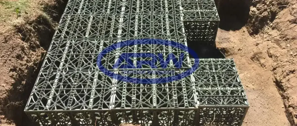 Cuenca de patio en construcción en Canadá: geomembrana negra con geotextil no tejido; un trabajador instala una tubería de drenaje perforada y la extensión vertical de una caja de captación.