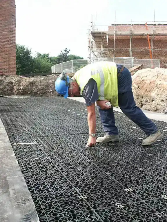 Un entrepreneur assemble des modules alvéolaires emboîtables pour former une couche de rétention des eaux pluviales sous une chaussée, destinée au drainage et à l’infiltration.