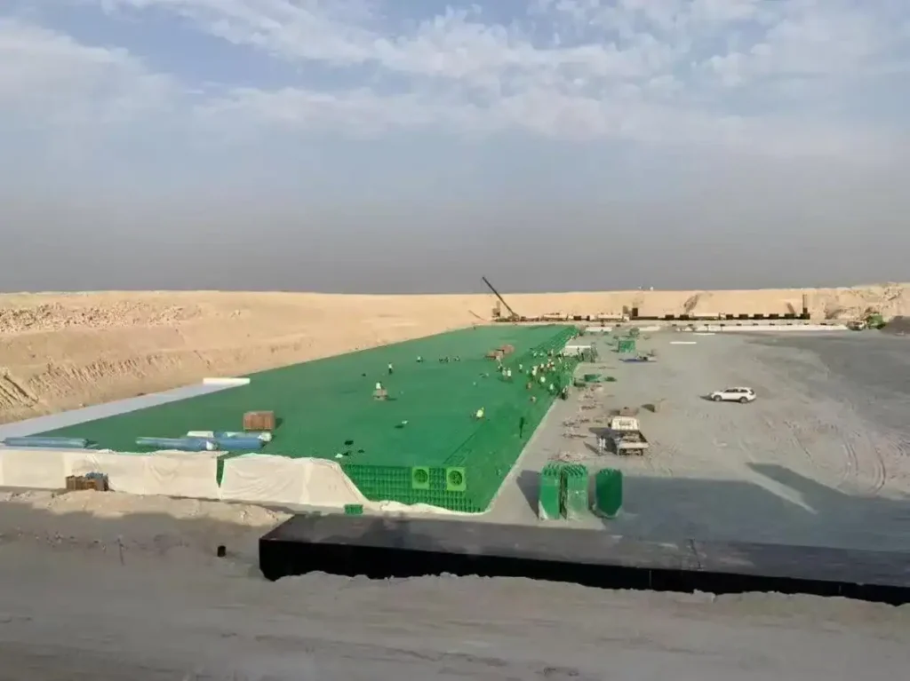 منظر جوي لخندق طويل يضم مساحات خضراء مزروعة بوحدات تخزين ذات بنية خلوية لتخفيف ذروة مياه الأمطار وتسرّبها إلى التربة في بيئة صحراوية.