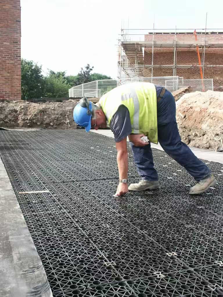 Módulos de atenuación geocelulares de polipropileno apilados en una obra junto a secciones de tanques de concreto prefabricado para mostrar las diferencias de tamaño y peso