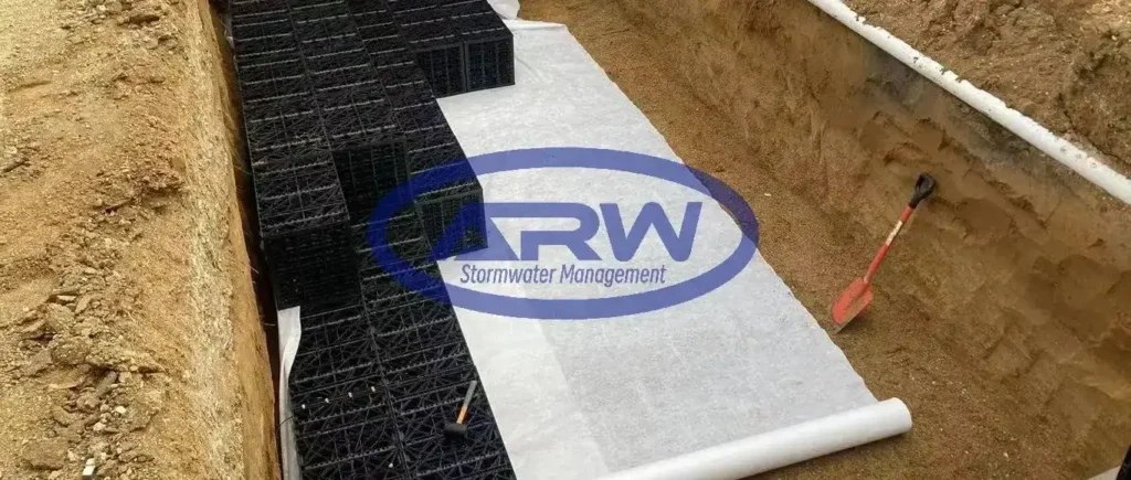 Installation d’un ouvrage résidentiel de rétention sur site (OSD) sur une petite parcelle en Australie et en Nouvelle-Zélande : fouille réalisée près de la maison, modules alvéolaires de stockage posés par étapes, rouleau de géotextile et conduites de raccordement.